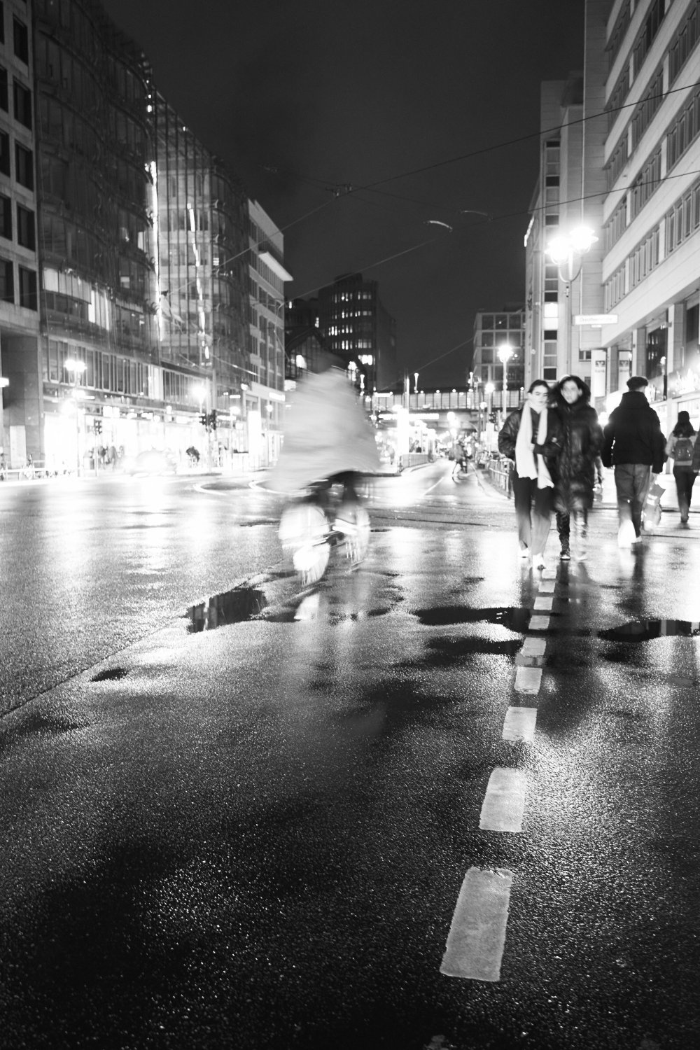 Nachtaufnahme der Friedrichstrasse in Berlin mit feuchtem Pflaster, Fußgängern und beleuchteten Gebäuden