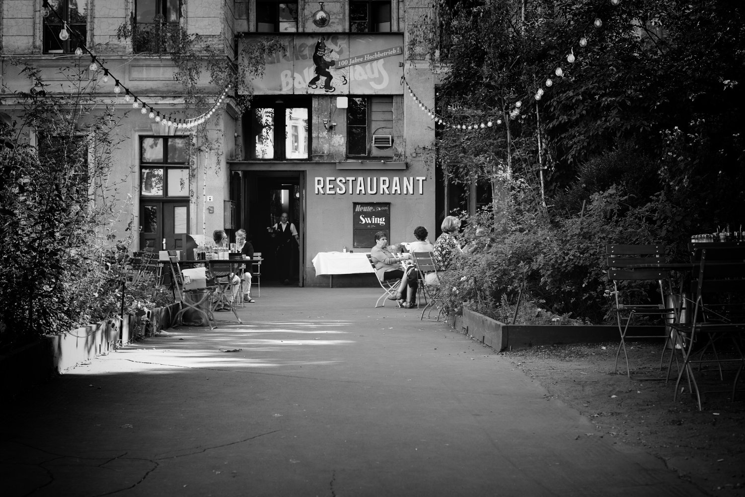 Schwarz-Weiß-Aufnahme des Restaurants Swing in Clärchens Ballhaus, Berlin Mitte, mit Gästen im Innenhof