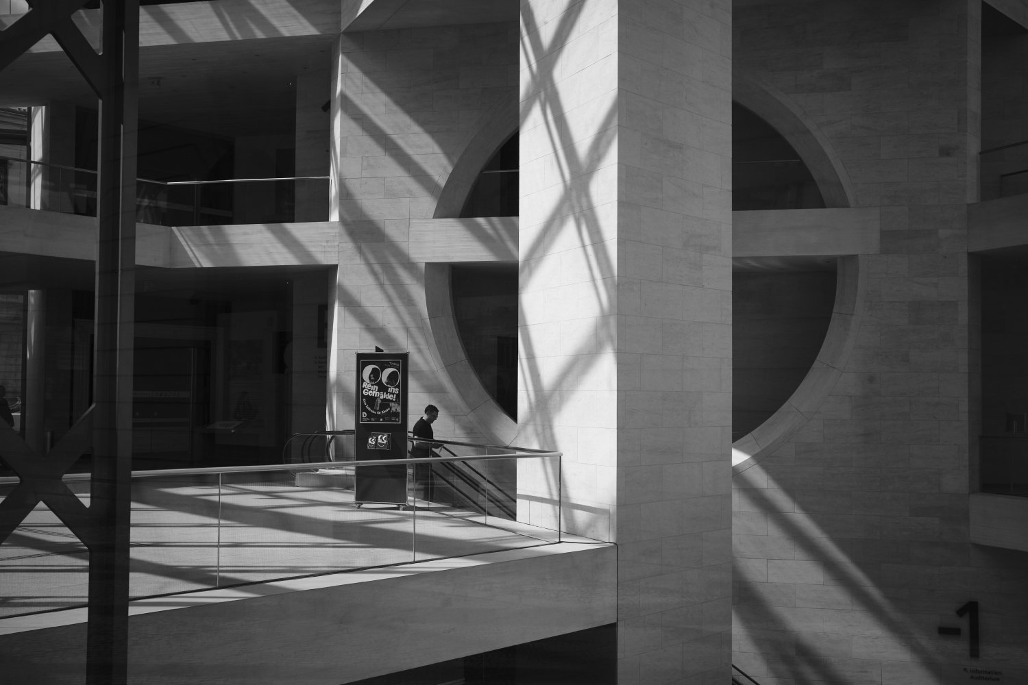 Single person standing in modern museum courtyard with geometric architecture and shadow patterns