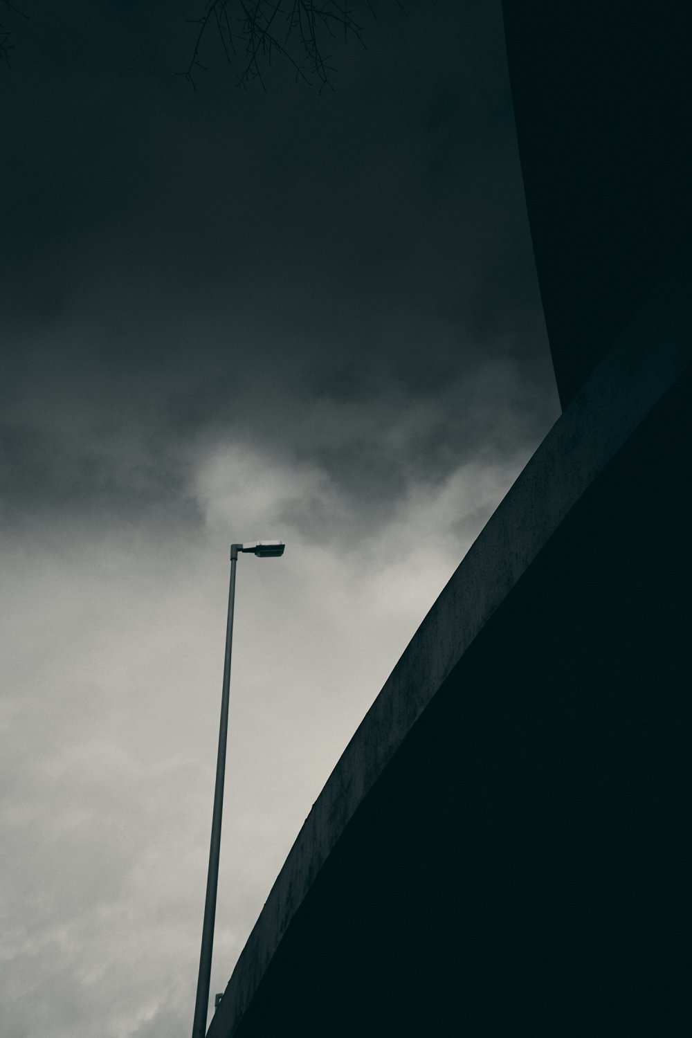 Street lamp against dramatic cloudy sky beside concrete highway bridge in Berlin Wilmersdorf